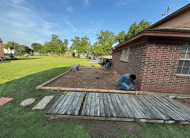 Worker leveling ground beside brick house