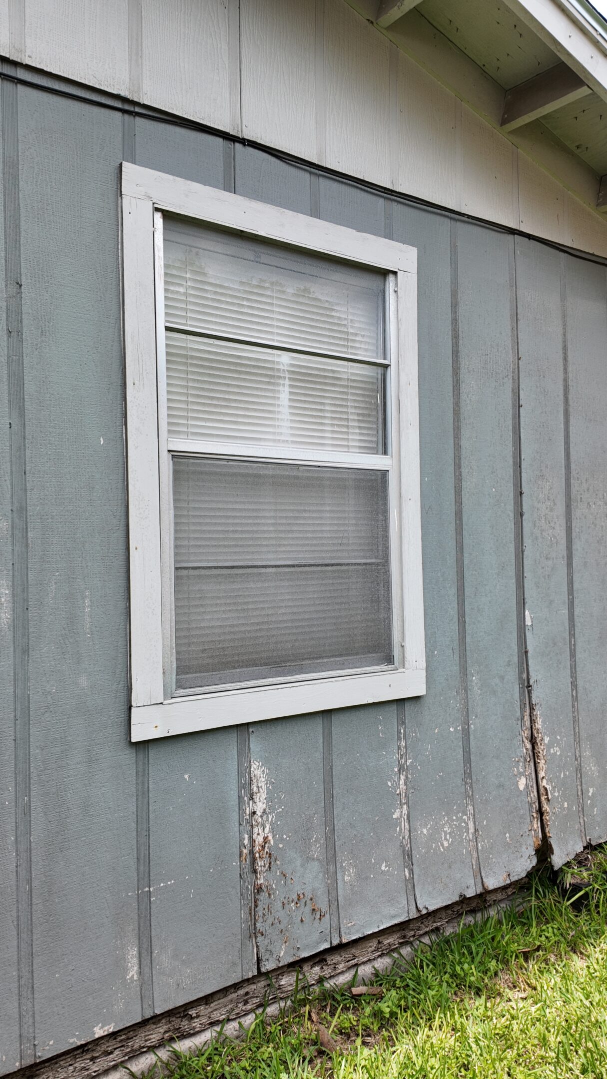 Old window with blinds on a weathered wooden wall.