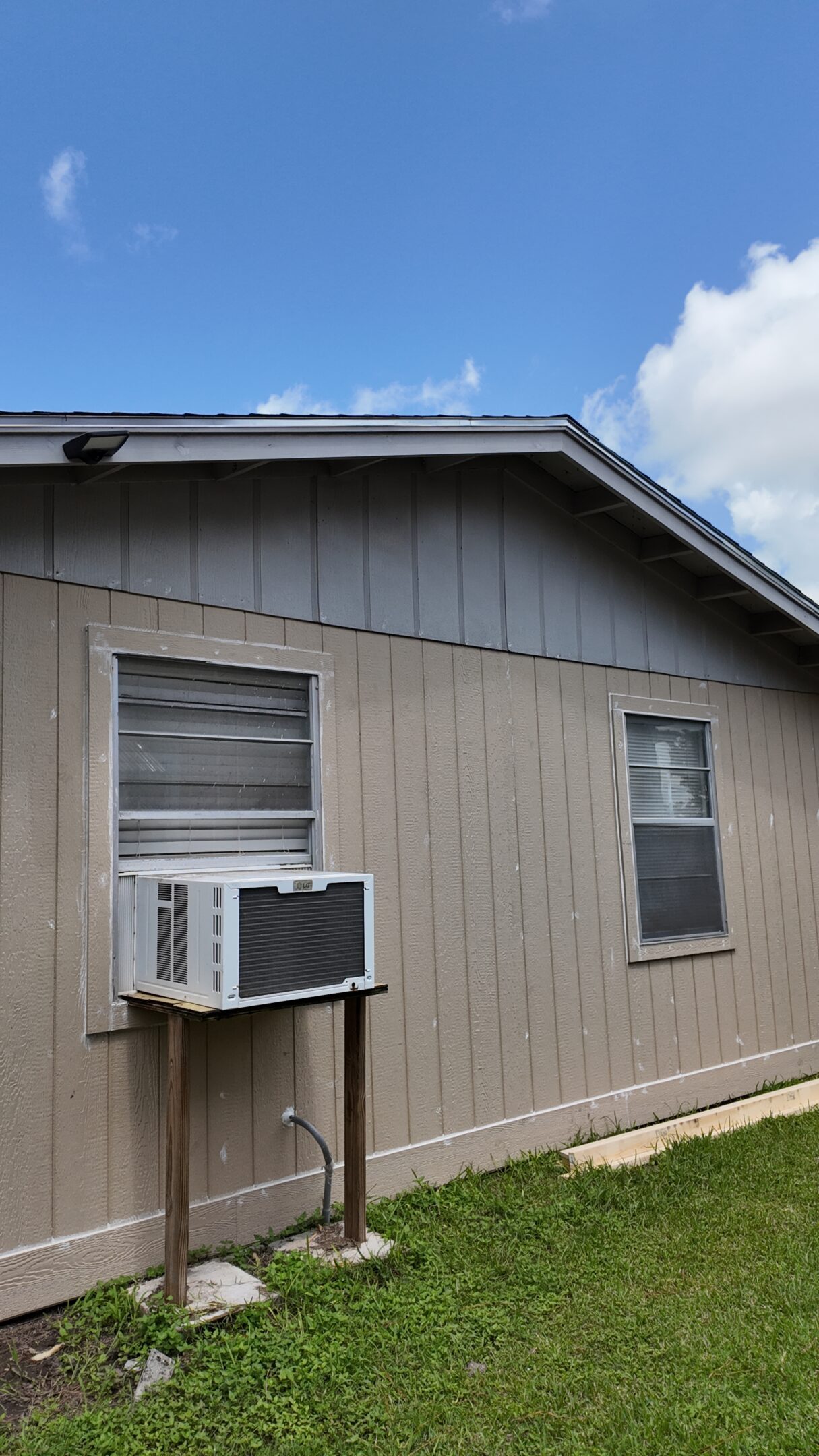 A beige house exterior with two windows and a window air conditioner unit.