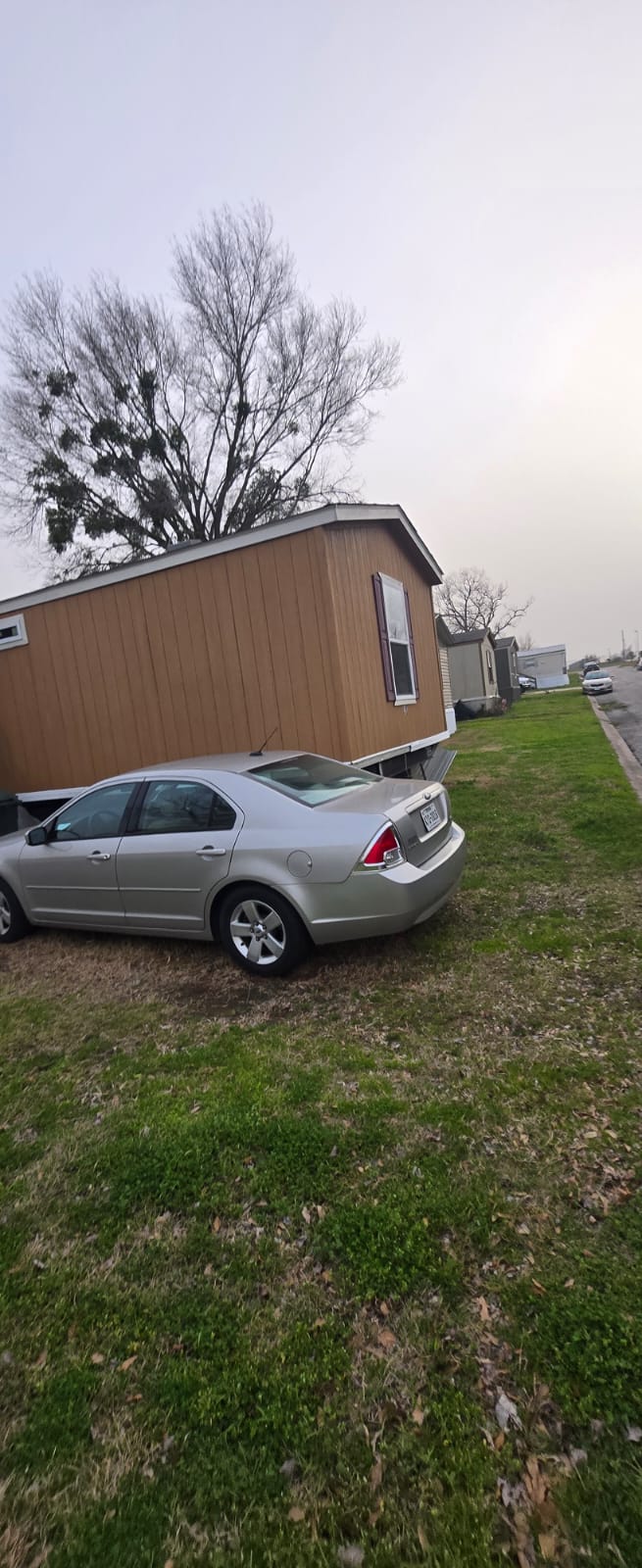 Silver sedan parked next to a brown mobile home on a grassy patch.