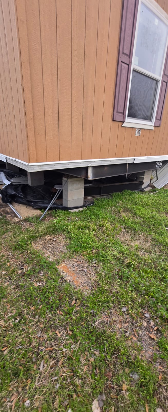 A house foundation with exposed supports and a grassy yard.