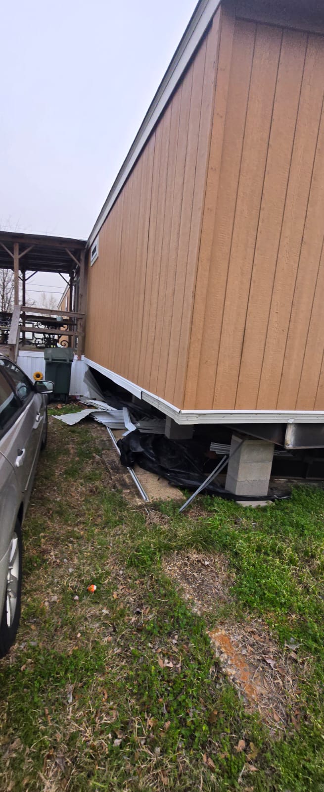 Damaged mobile home with detached skirting and debris on the ground.