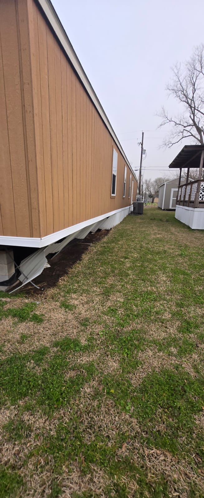 Raised wooden house with space underneath and grassy yard beside it.