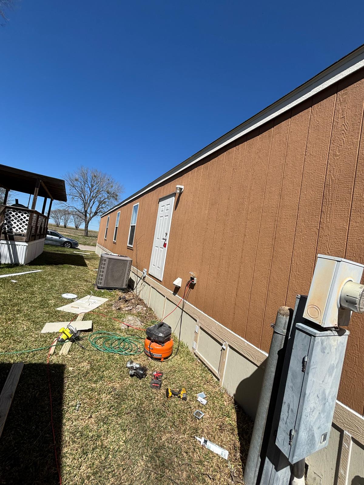 Side view of a brown building with scattered outdoor items and a clear sky.