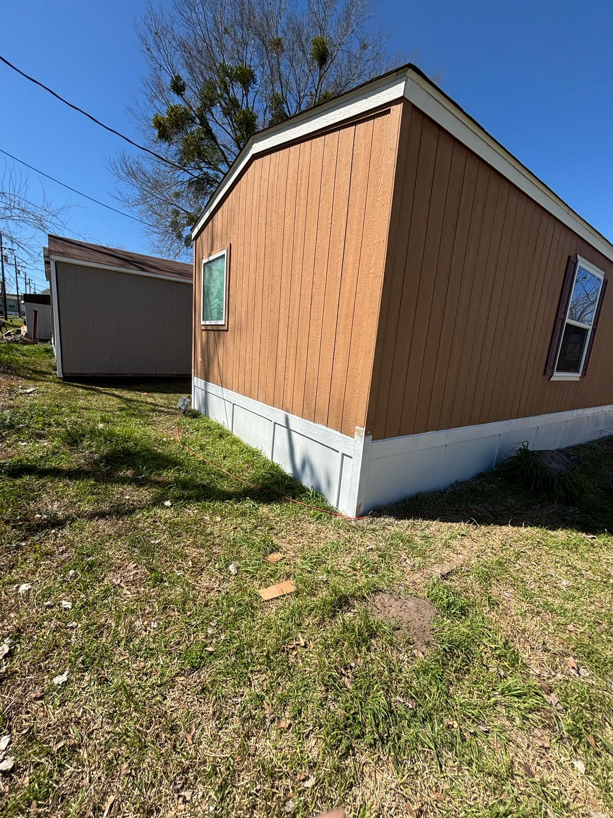 Two brown shed-like buildings on grassy ground under a clear blue sky.