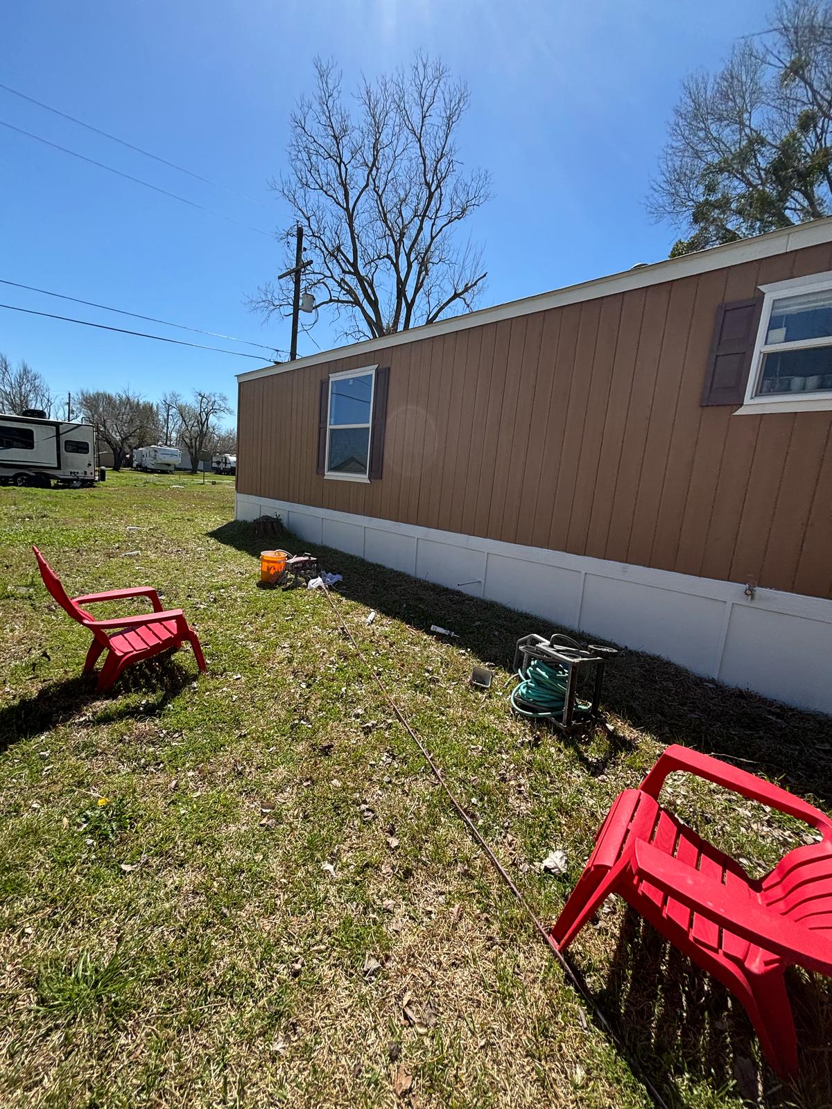 Backyard with red chairs and a brown mobile home under clear blue sky.