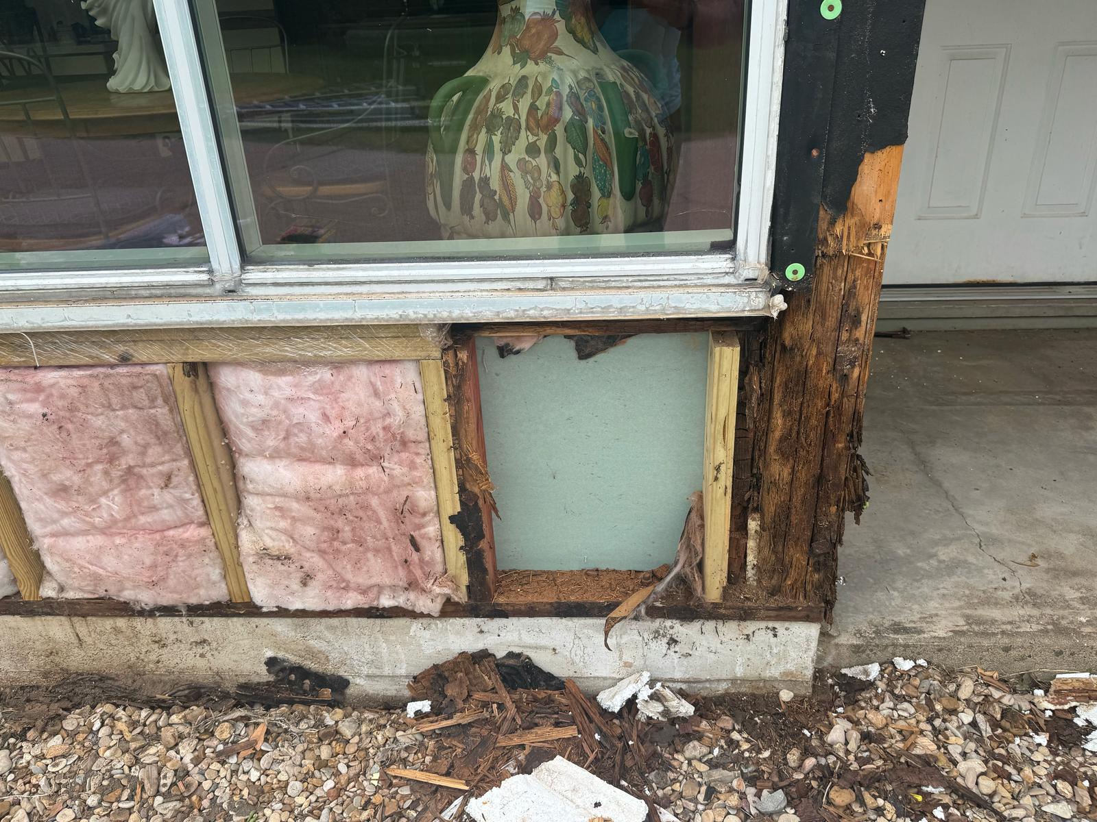 A damaged window frame with peeling paint and insulation visible.