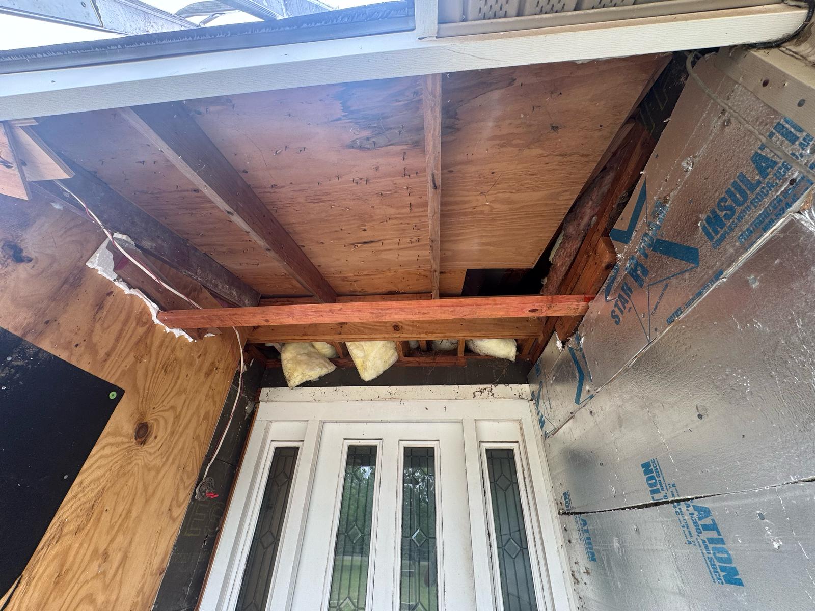 Damaged ceiling above a door with exposed wooden beams and missing panels.