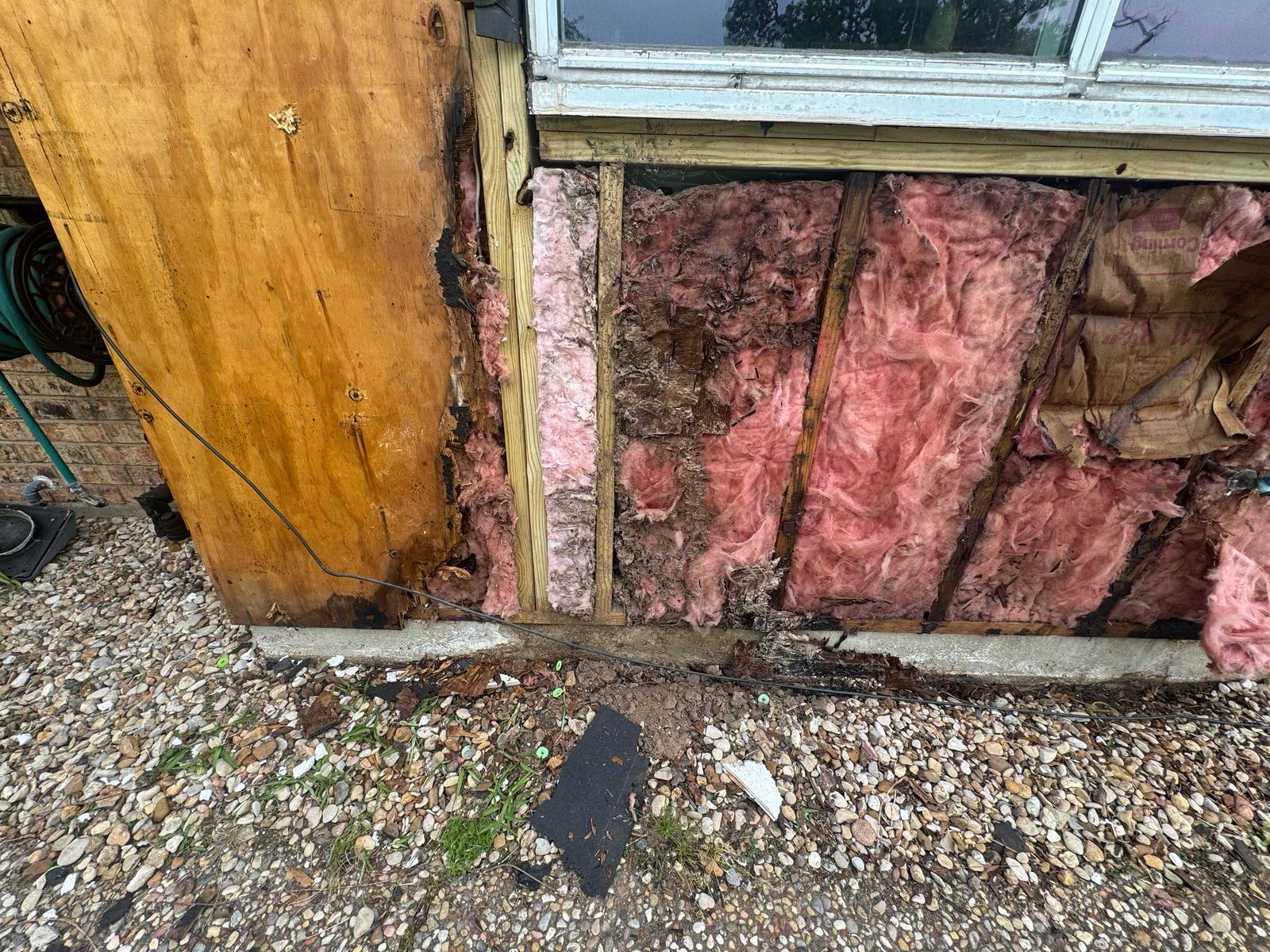 Exposed pink insulation and rotting wood near a window on a building exterior.