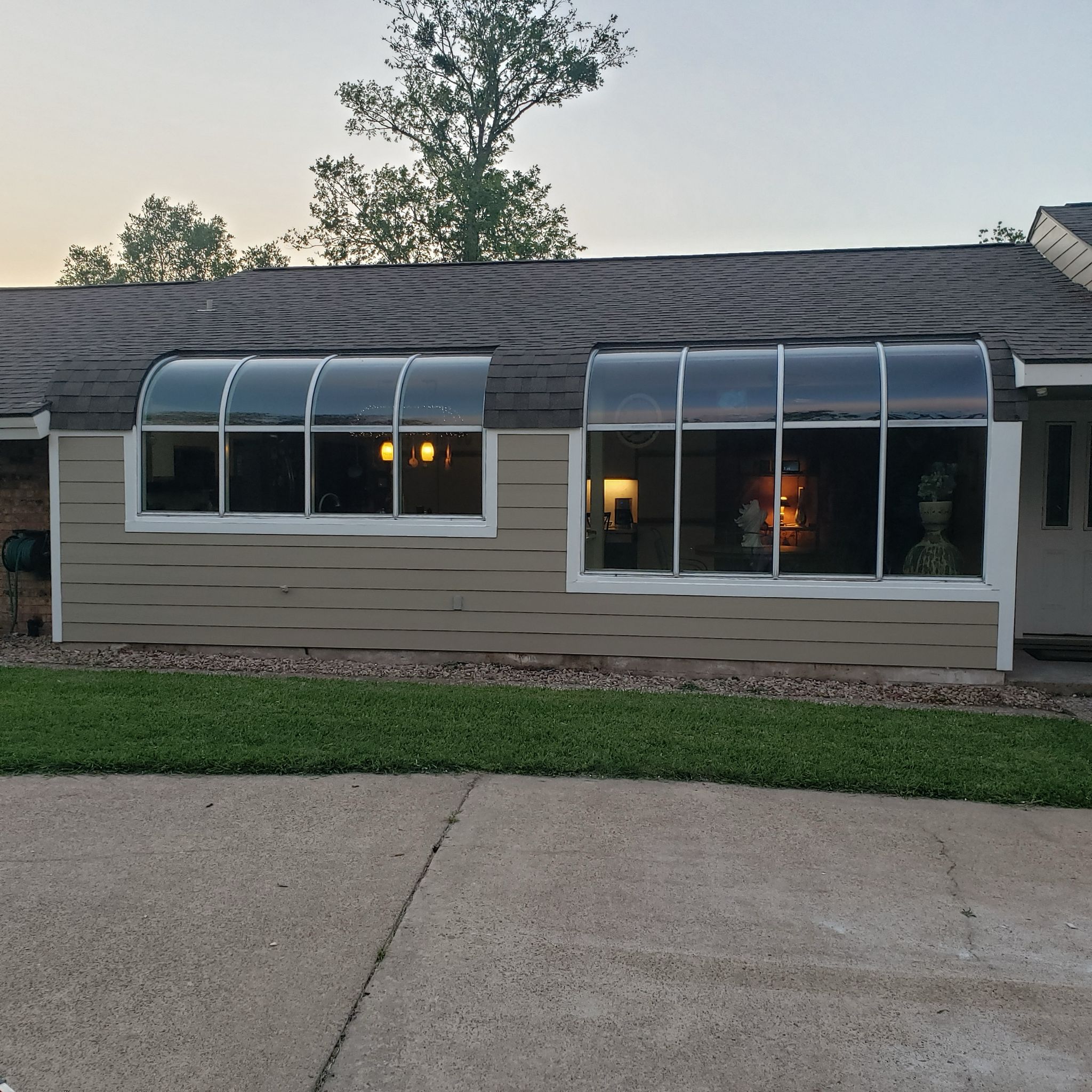 A suburban house with large windows and a well-kept lawn at dusk.