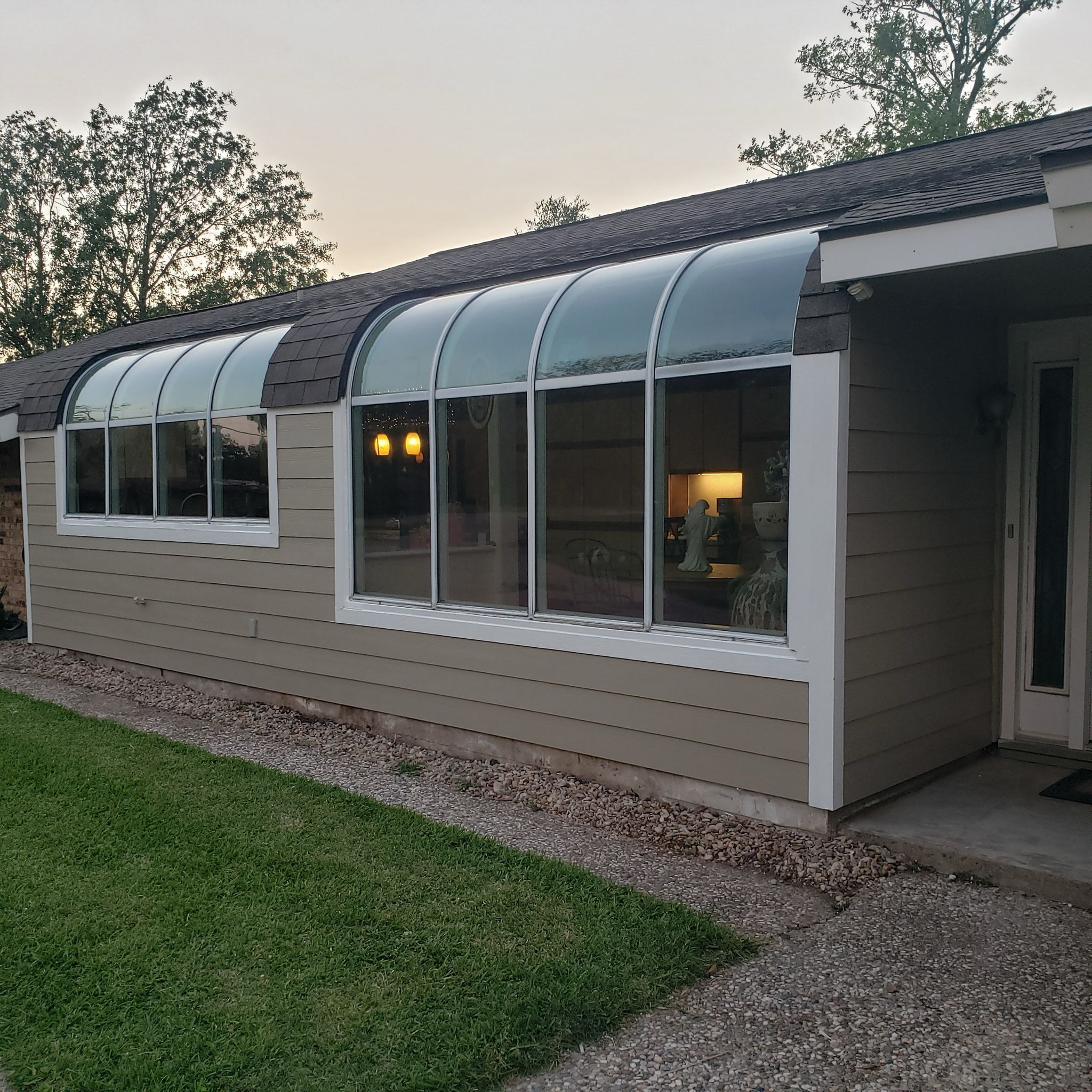 A house with large arched windows and beige siding at dusk.