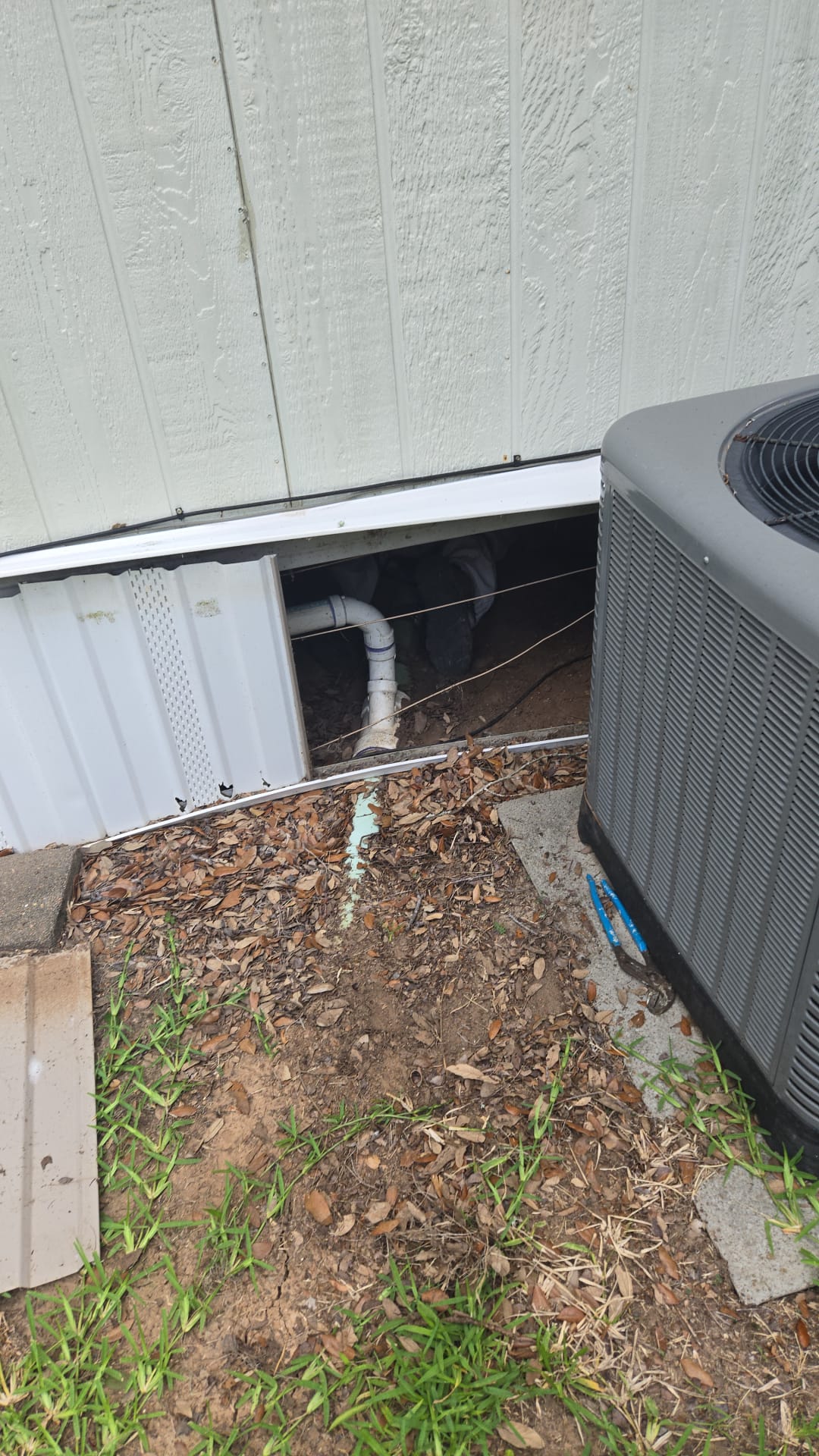 Outdoor air conditioning unit with exposed pipes and soil area.