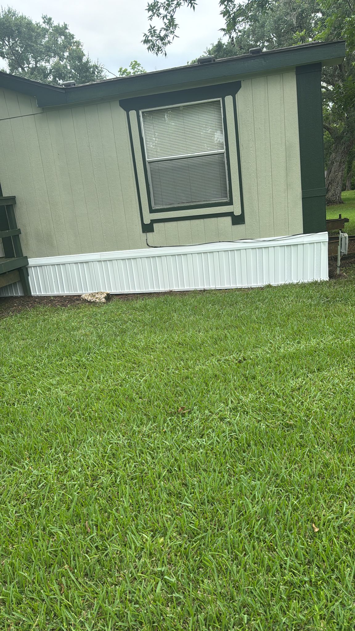 A grassy yard in front of a mobile home with a boarded window.