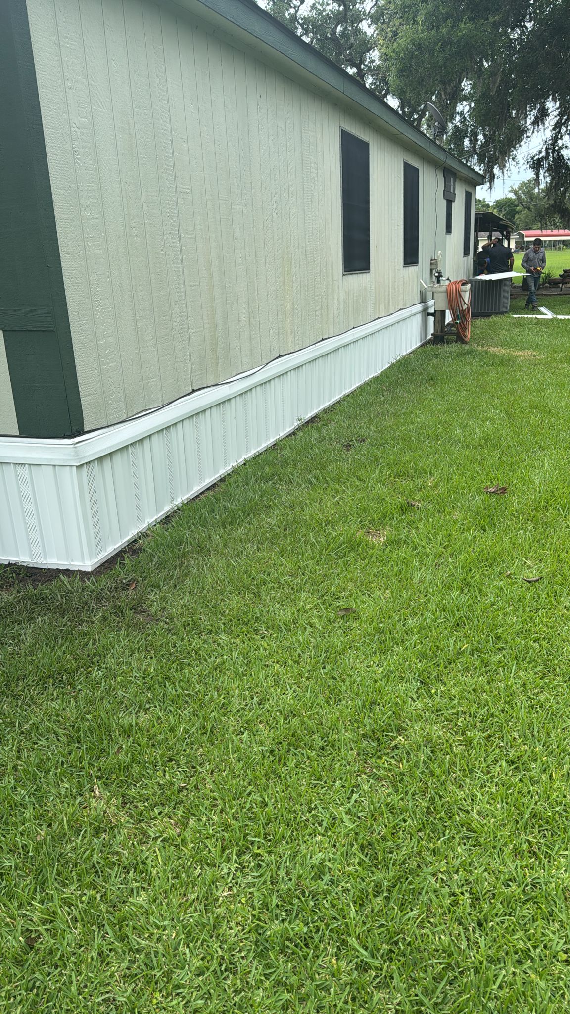 White skirting installed along the base of a mobile home on green grass.