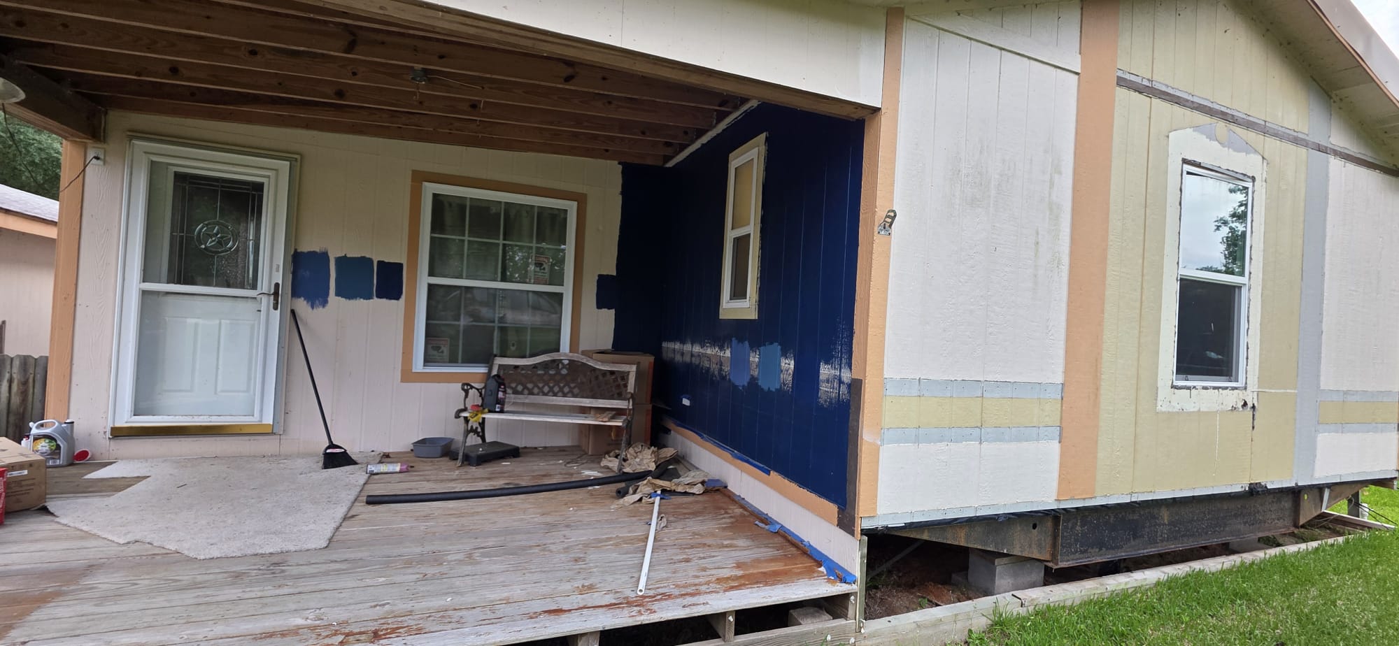 Partially painted house exterior with a porch swing and construction materials.