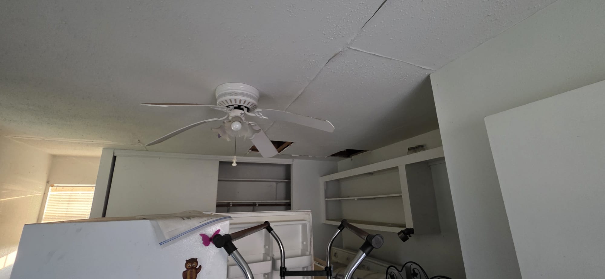 Ceiling fan with damaged blades in a room with shelves and equipment.