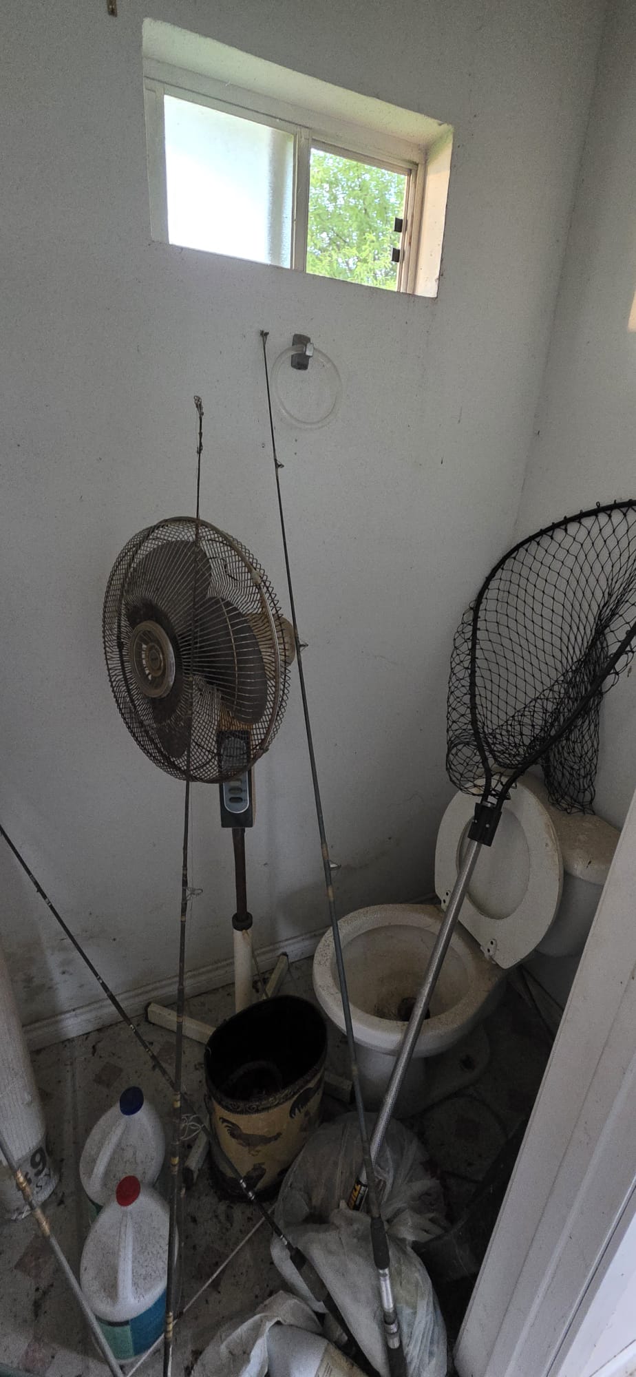Fishing rods and net stored next to a standing fan in a corner.
