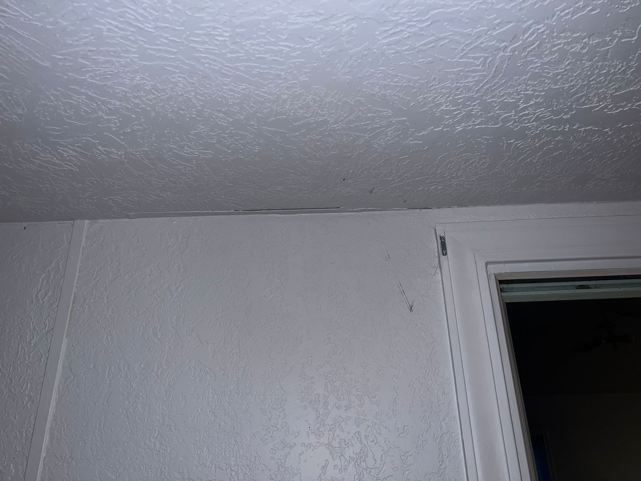 Cracks and peeling paint on a white interior wall near a ceiling and door frame.