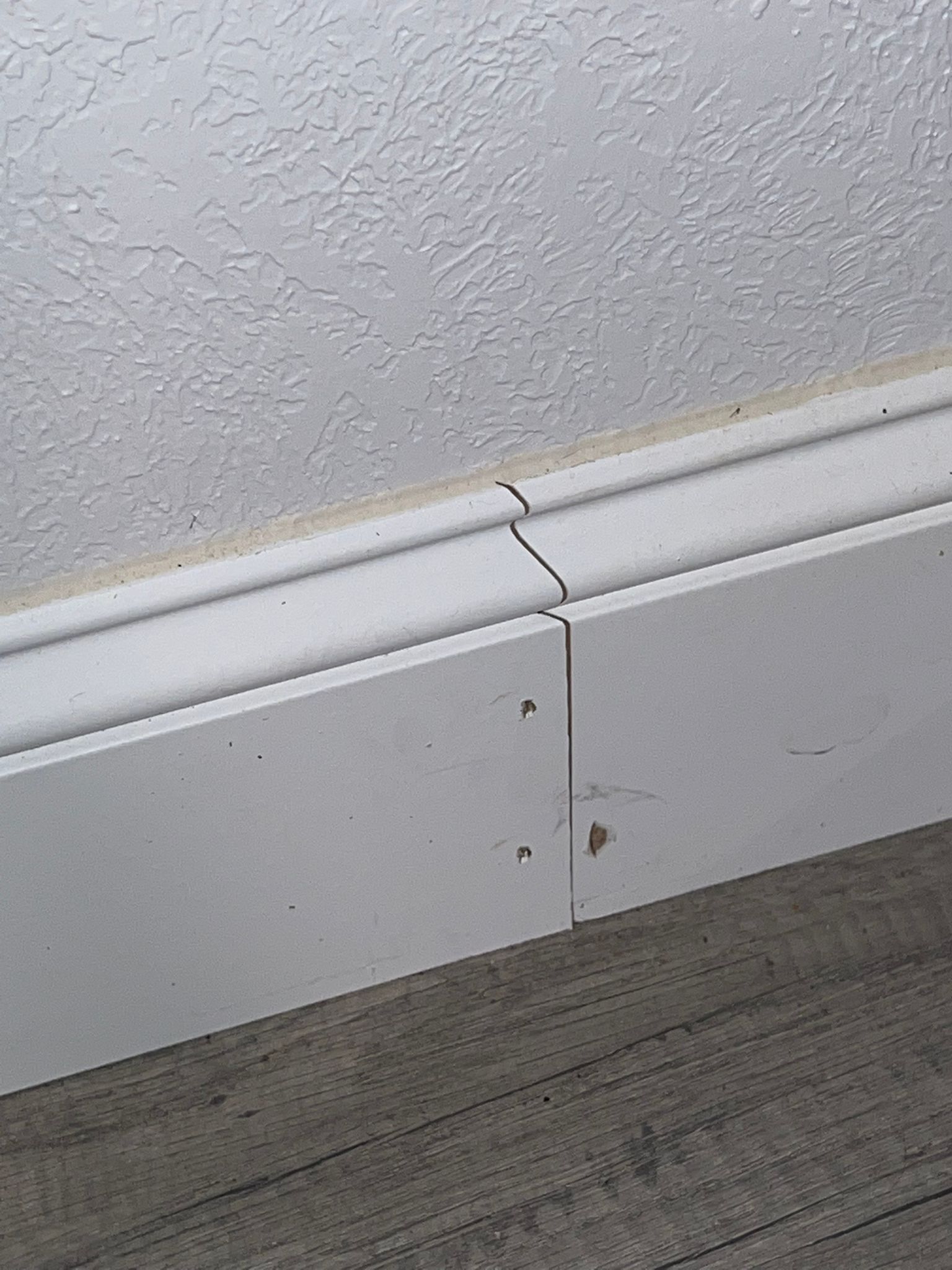 Close-up of a split white baseboard with visible nails and cracks.