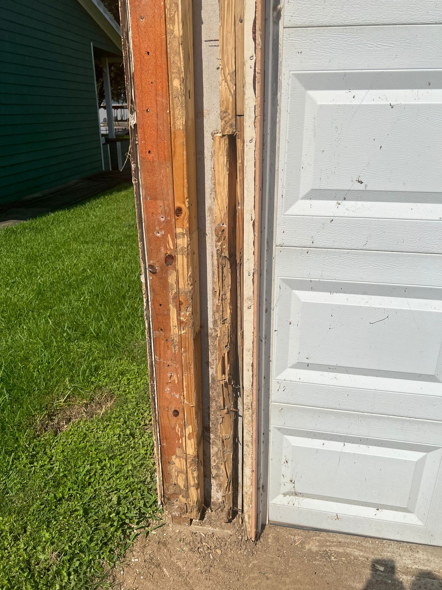 Close-up of damaged wooden door frame beside a white garage door.