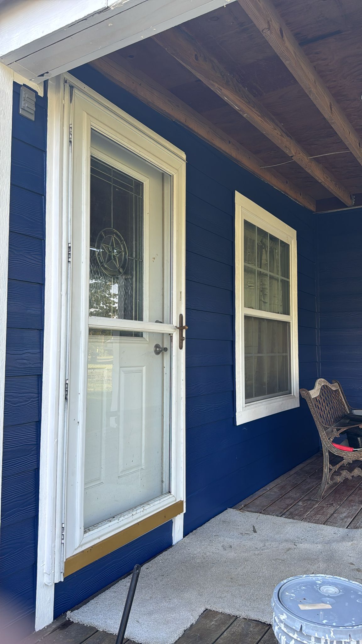 White door and window on a blue house exterior with a chair nearby.