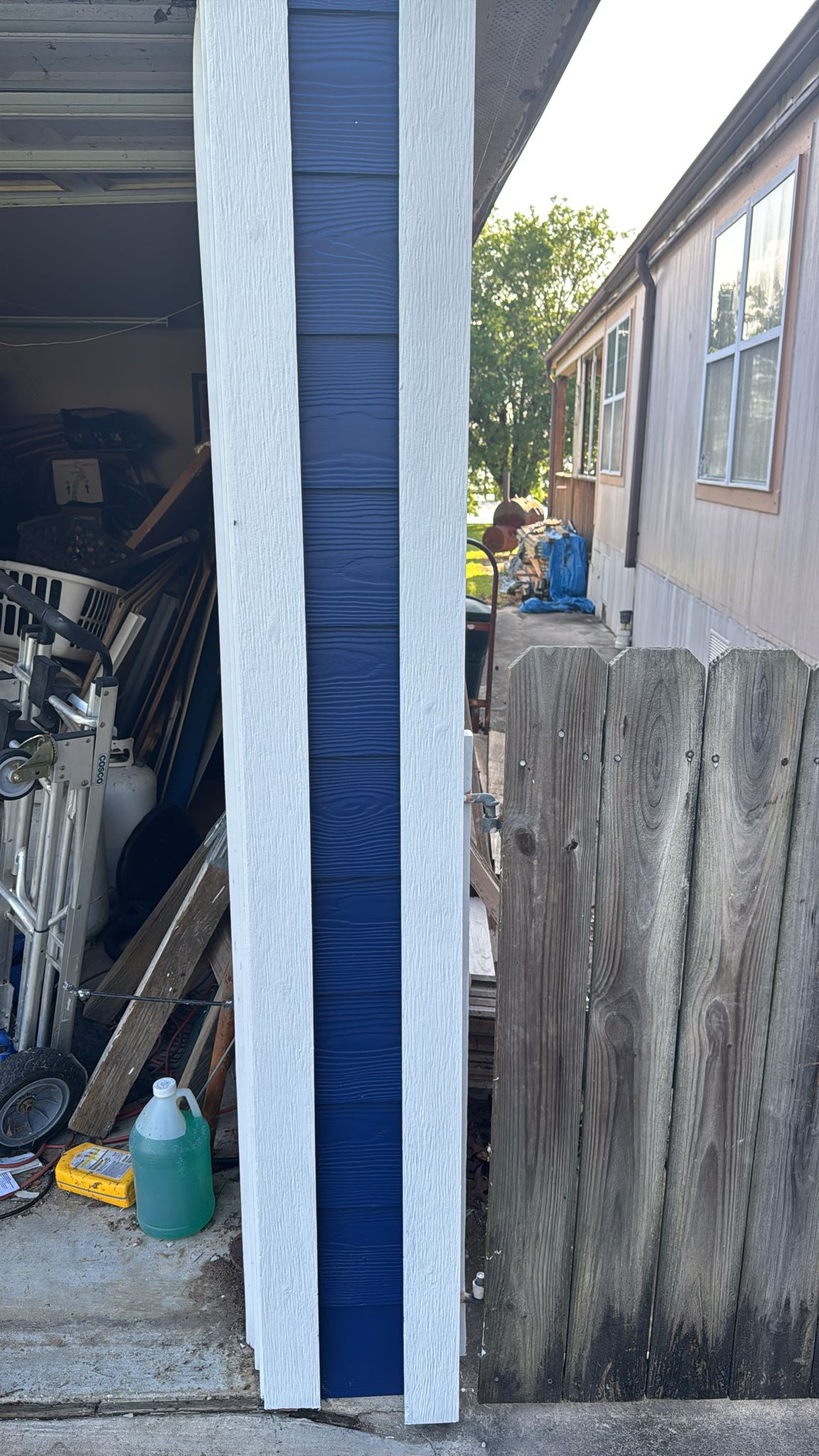 A narrow gap between a blue and white building and a wooden fence.