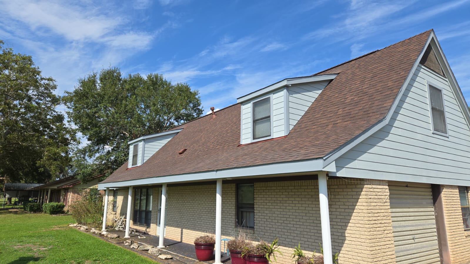 A suburban house with a brown roof and dormer windows under a blue sky.