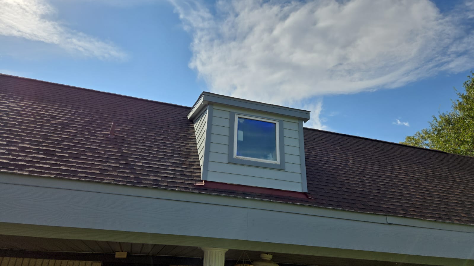 A dormer window on a sloped roof under a partly cloudy sky.