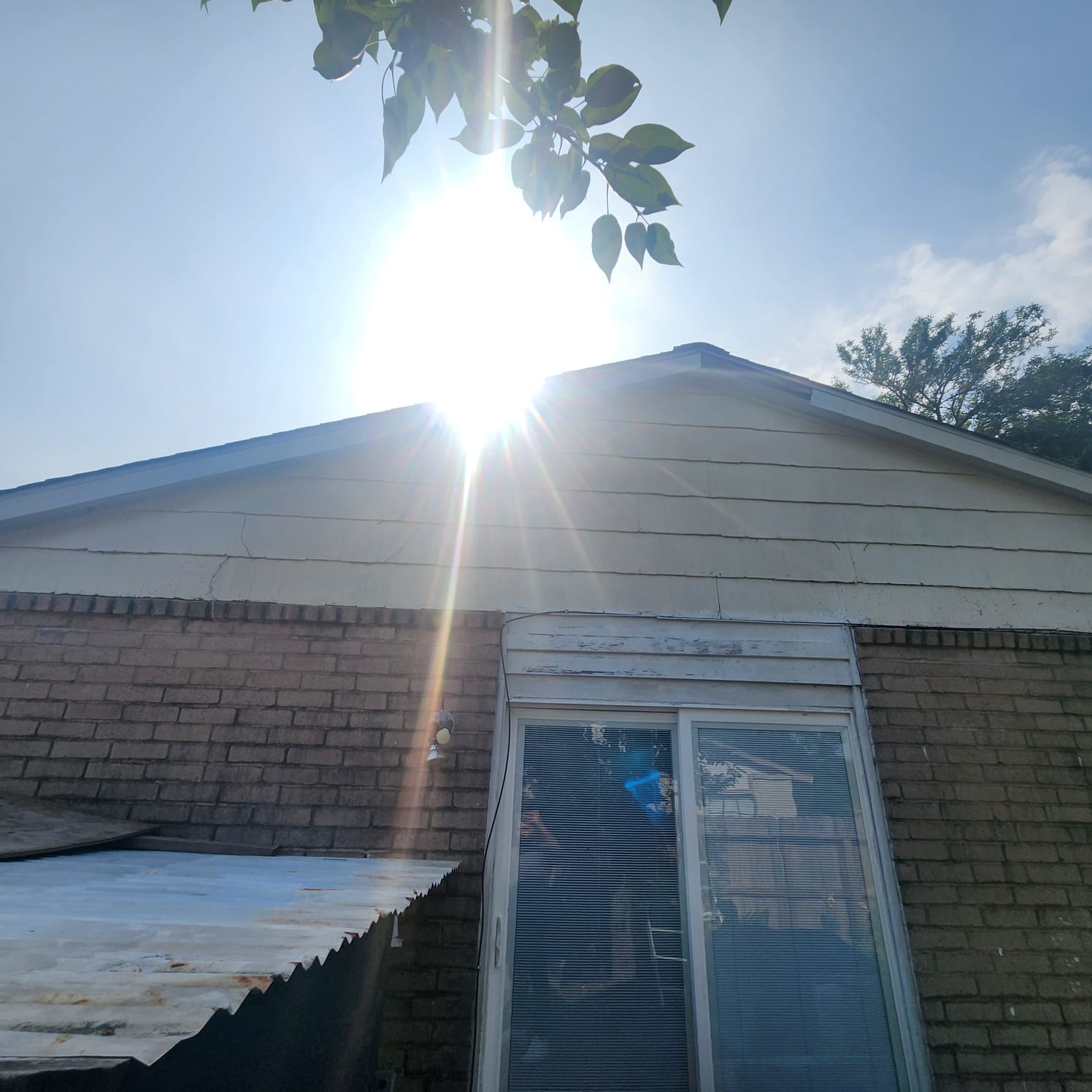 Sunlight shines brightly over a brick house with a window and leafy branches above.