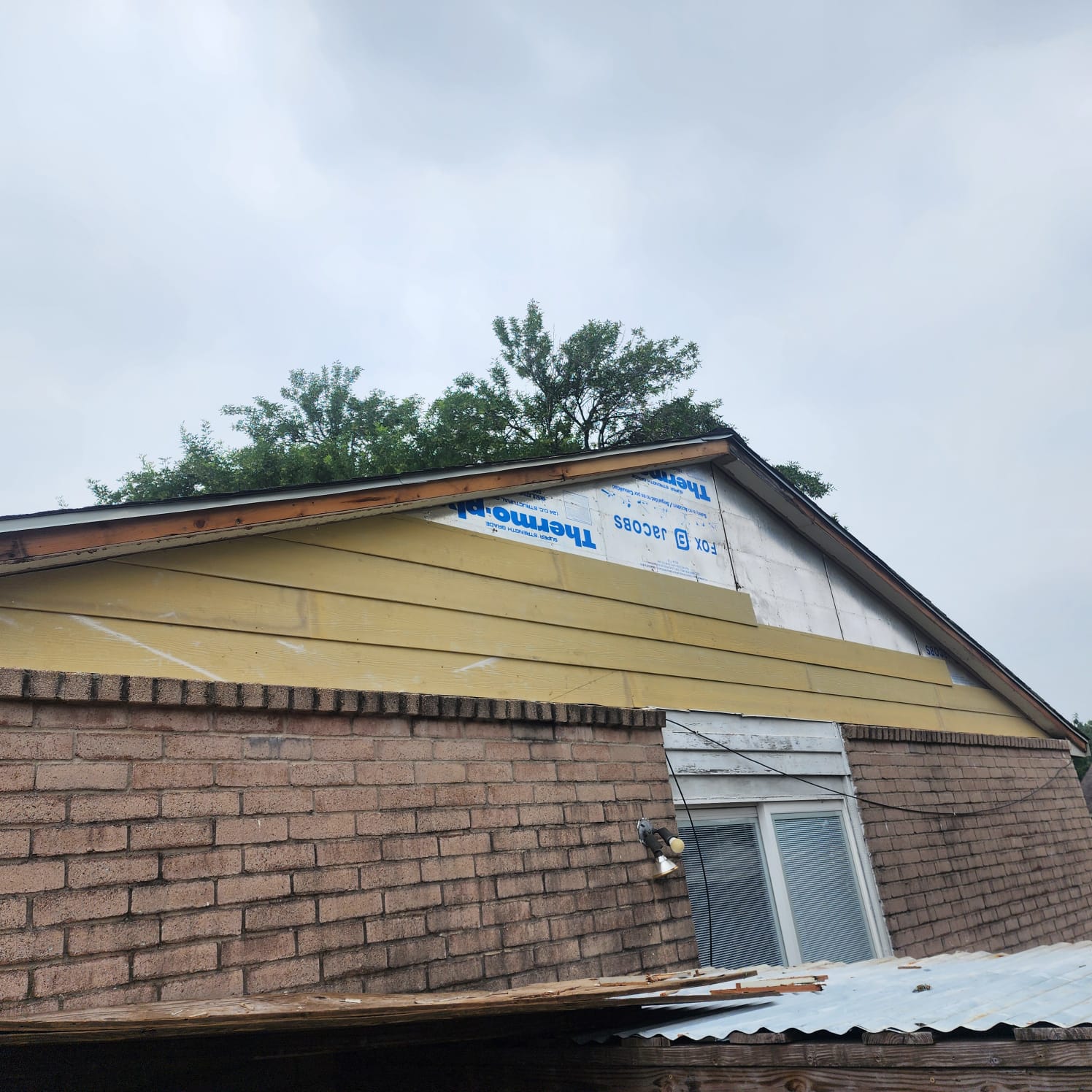 A house roof under renovation with new yellow siding and brick walls.