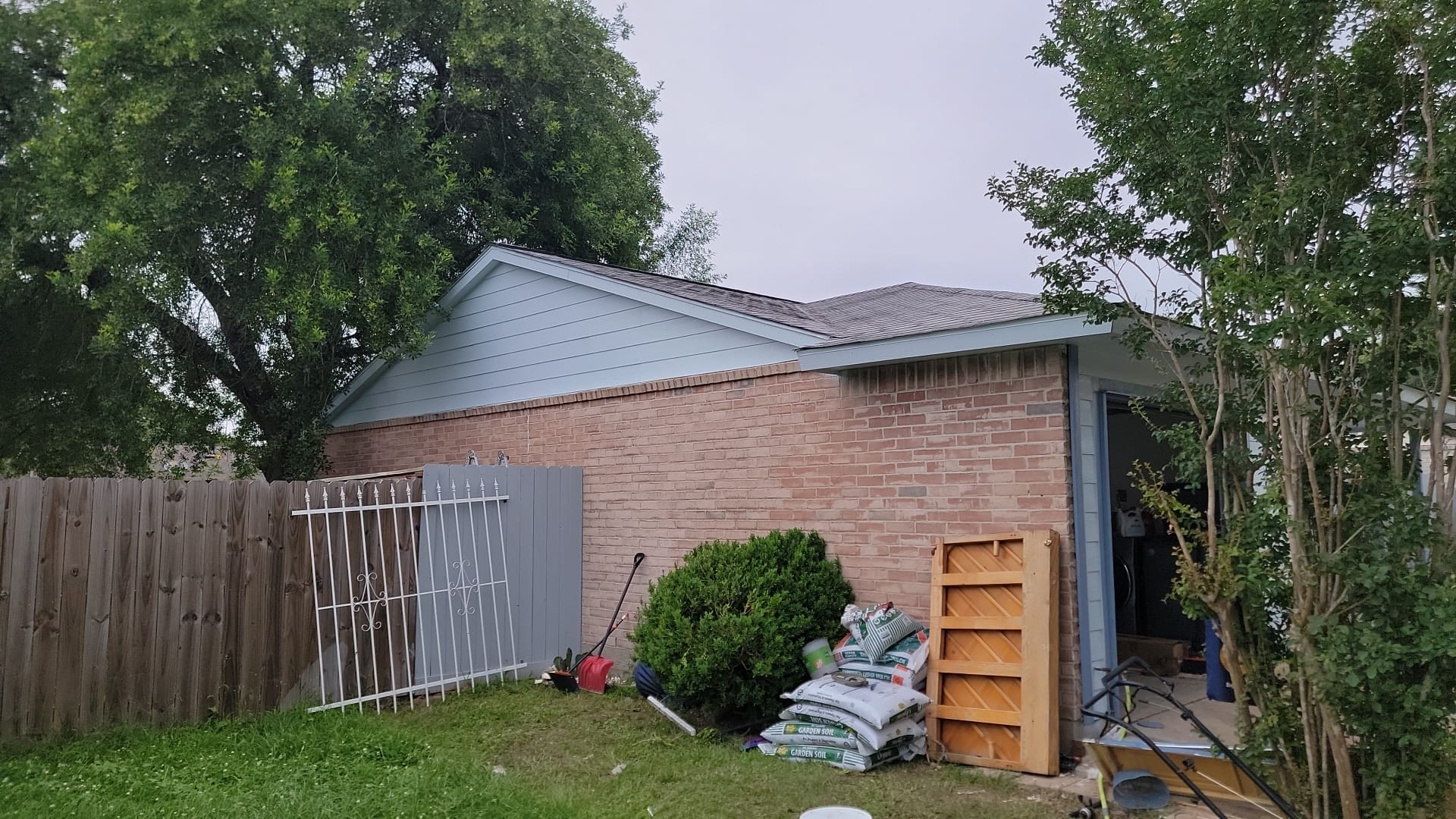 A brick house with gardening tools and bags near a fence.