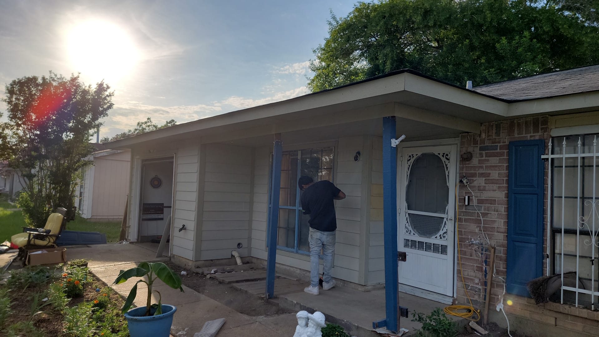 Person painting blue posts on a house porch during daytime.
