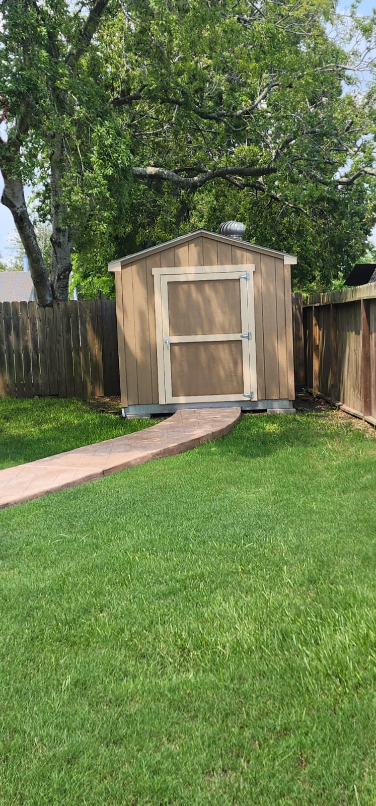 A wooden garden shed with a paved pathway in a green backyard.