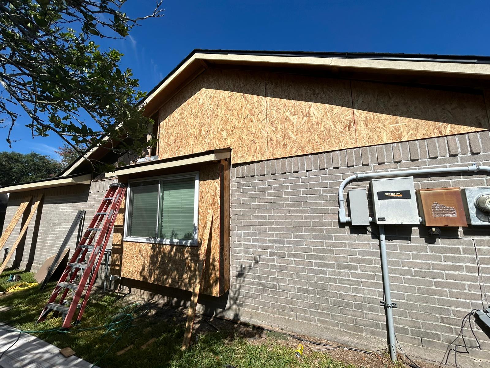 House exterior under renovation with plywood and ladder.