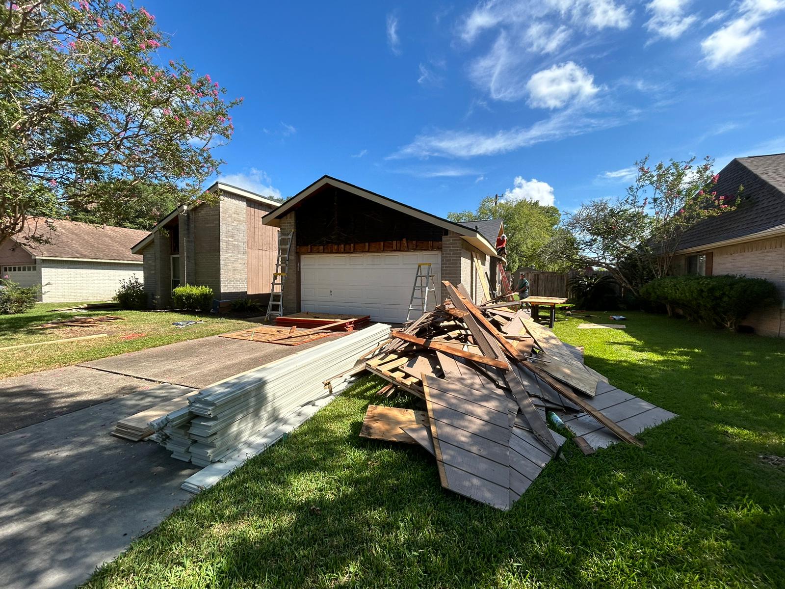 House with construction debris piled in the driveway on a sunny day.