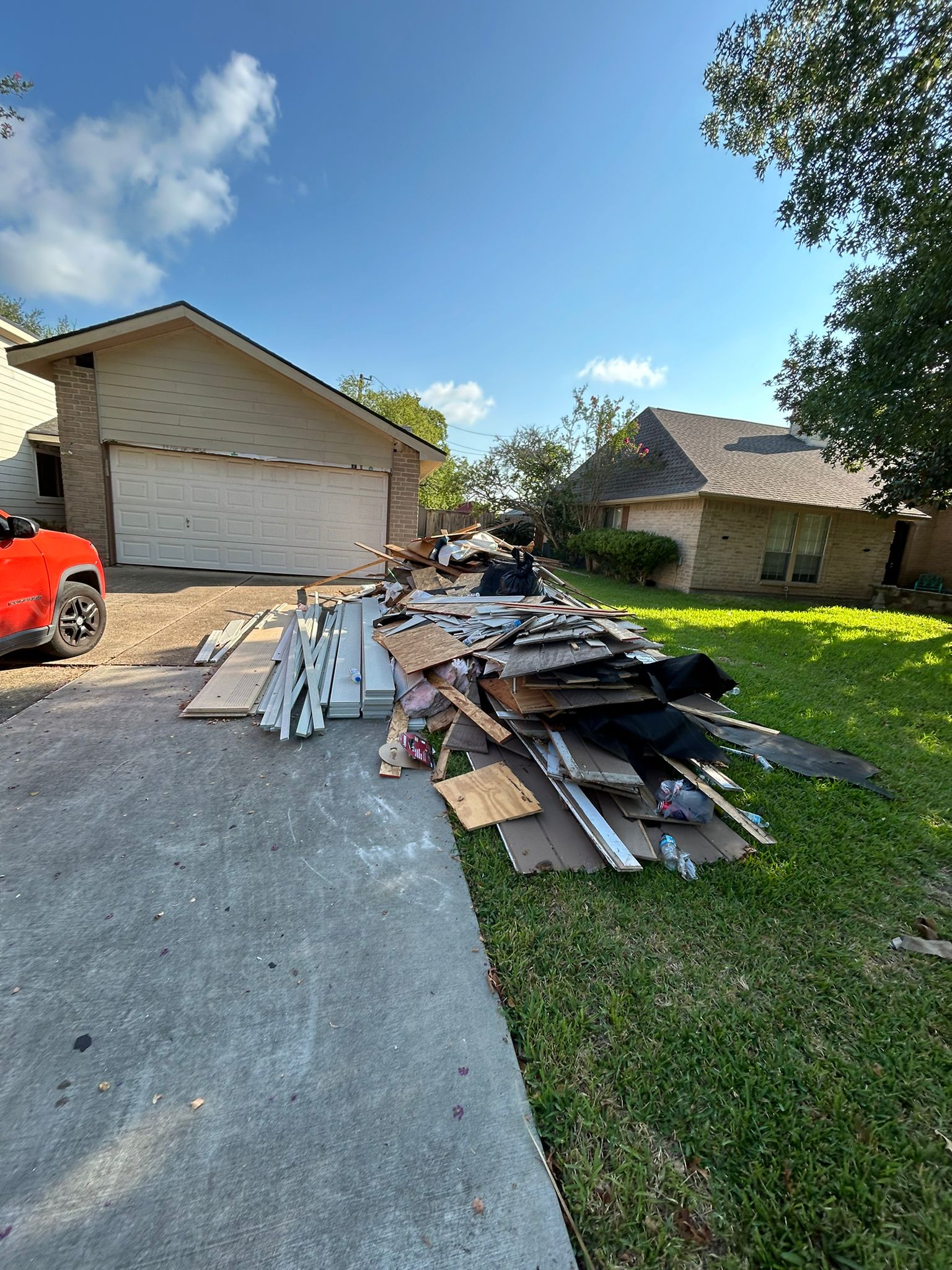 Pile of construction debris on a driveway beside a red truck and a house.