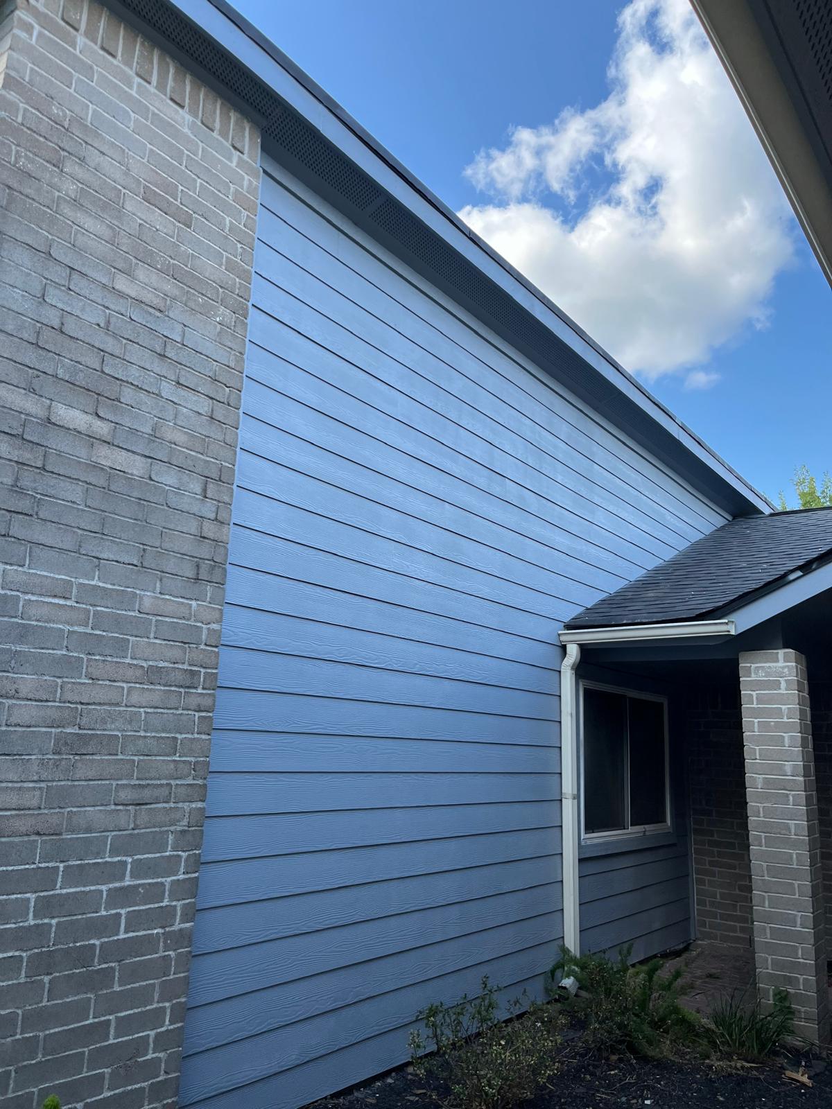 Blue siding wall with brick pillars under a partly cloudy sky.