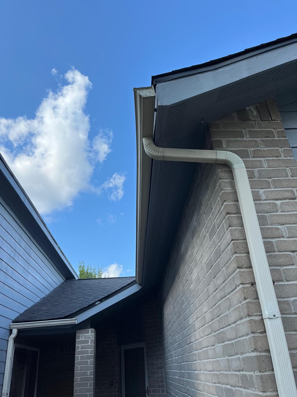 View of a house roof and gutter against a blue sky with clouds.