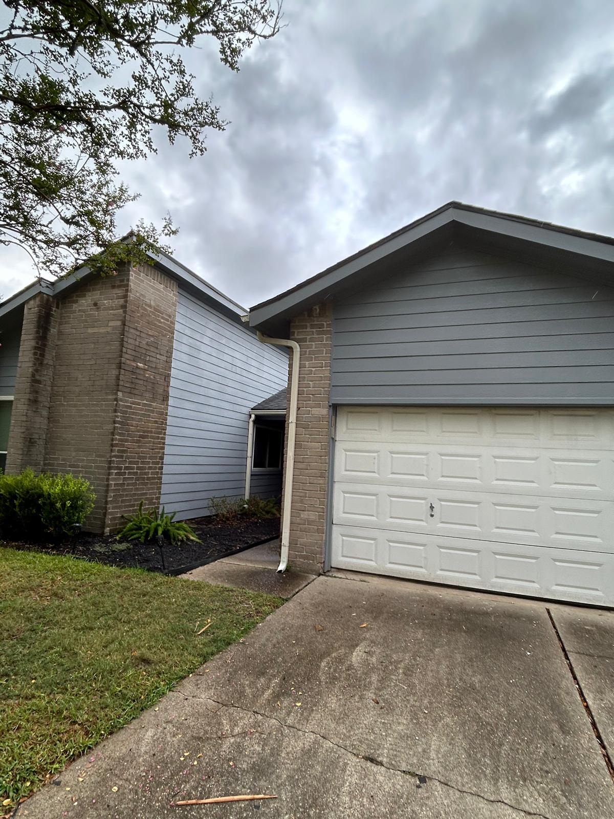 Two suburban houses with gray siding under a cloudy sky.