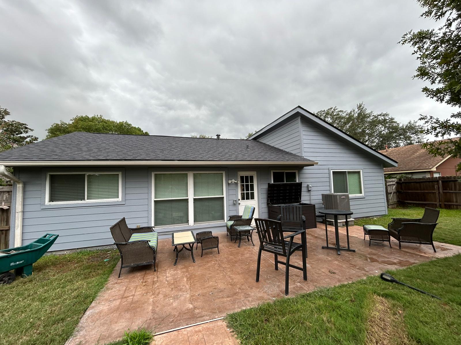 A single-story blue house with a patio and outdoor seating under a cloudy sky.