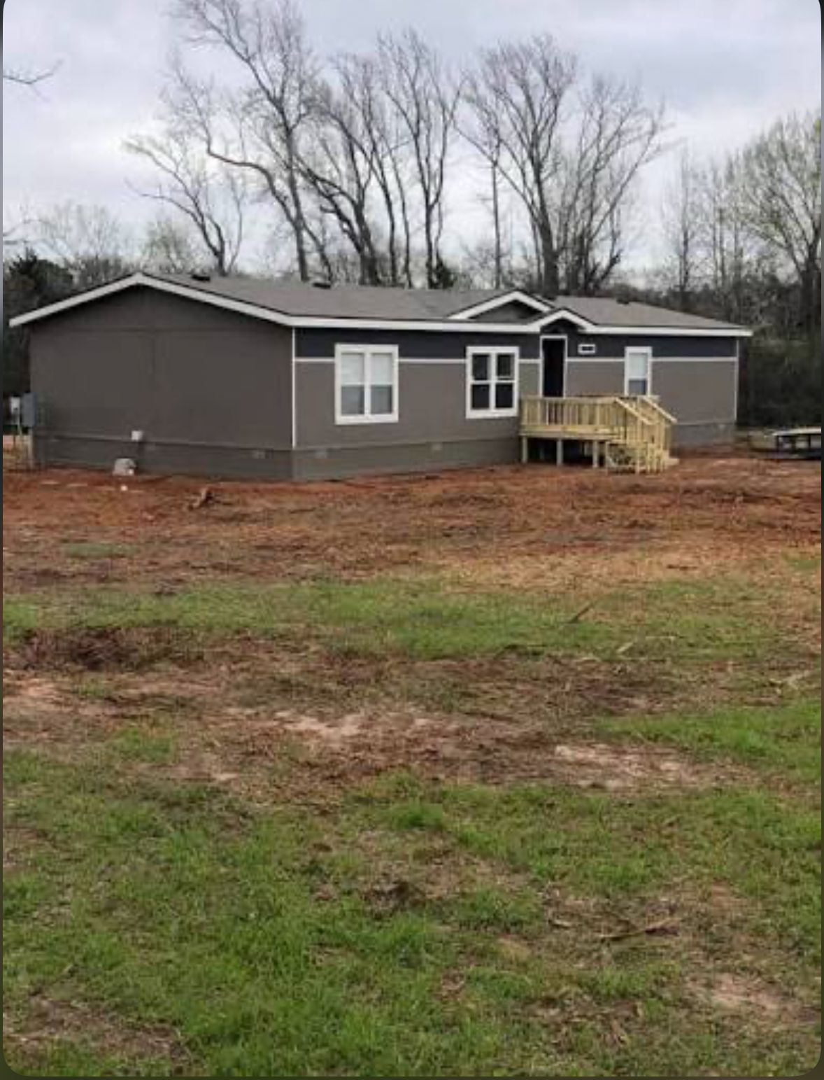 A gray single-story house with a small wooden deck under cloudy skies.