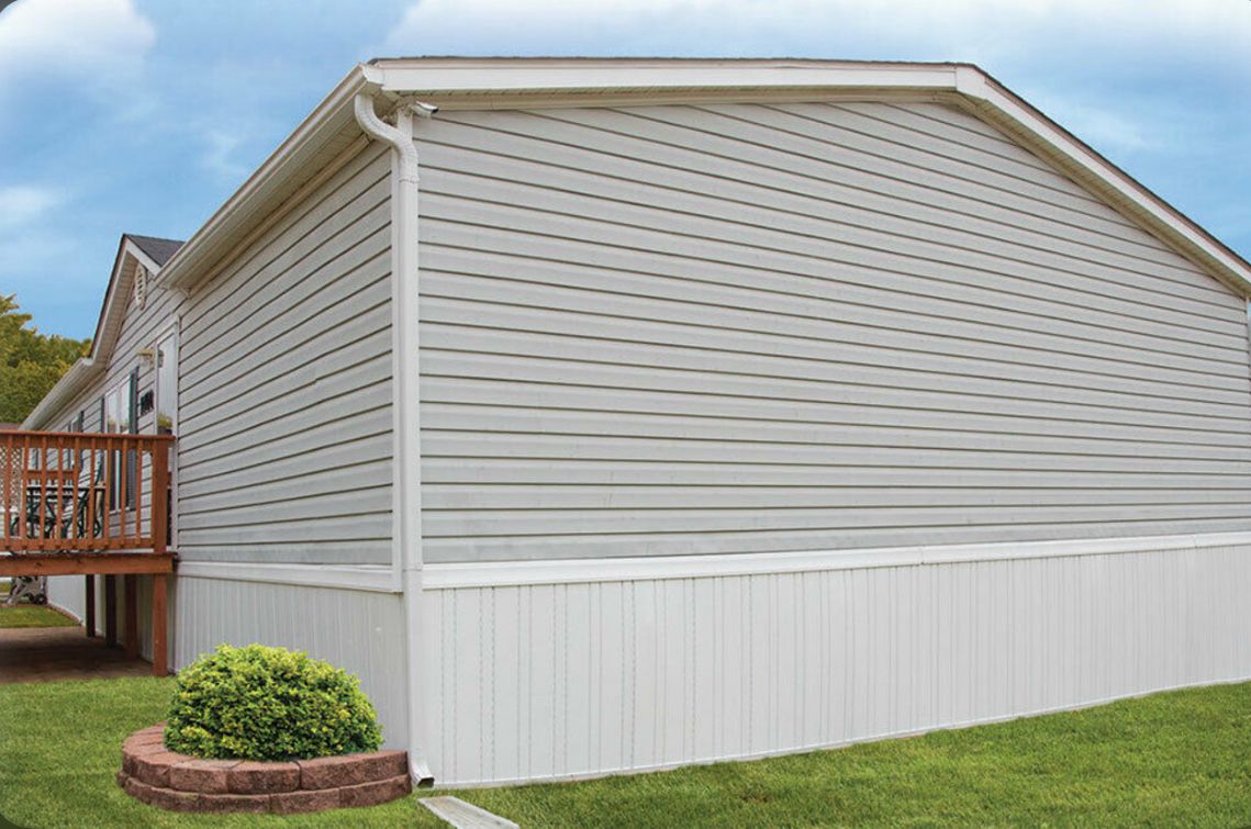 Side view of a beige mobile home with vinyl siding and gutter system.