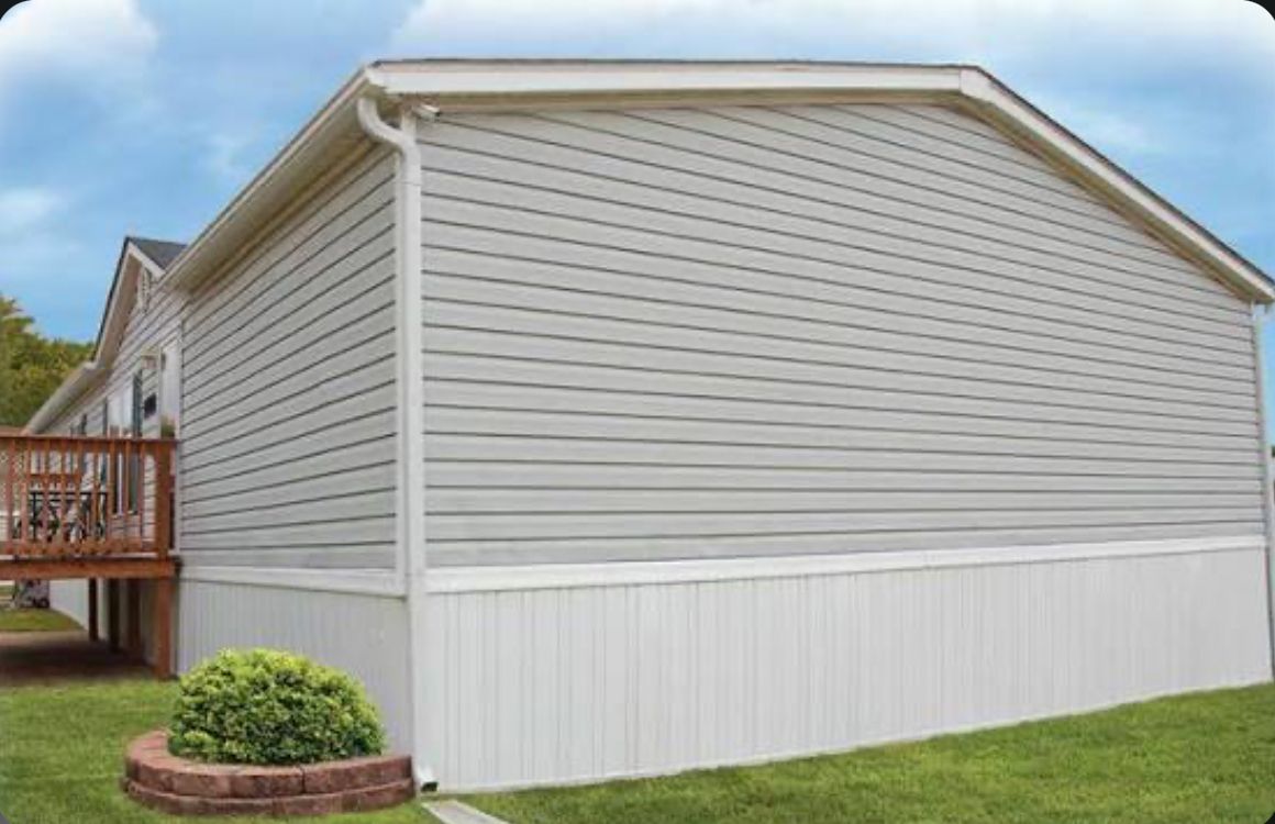 Side view of a gray mobile home with white trim and a small garden bed.