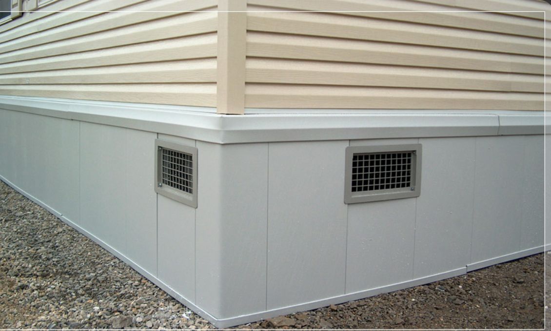 Gray foundation with vents beneath beige siding on a building corner.