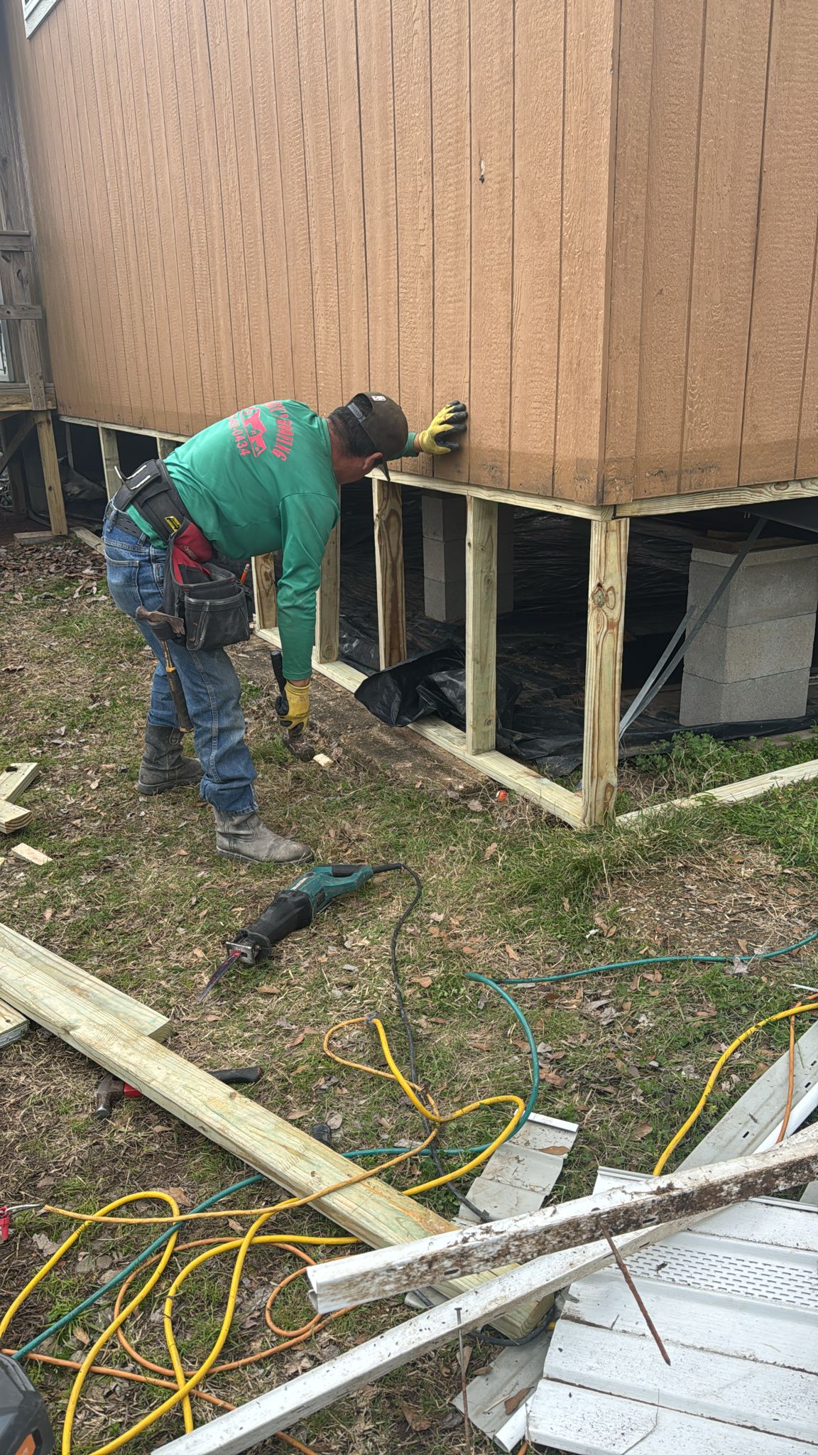 Man repairing wooden porch foundation outdoors.