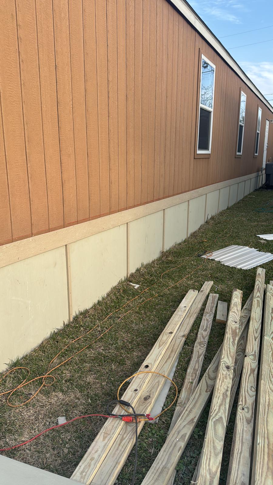 Wooden planks and white panels lie on the grass beside a building.