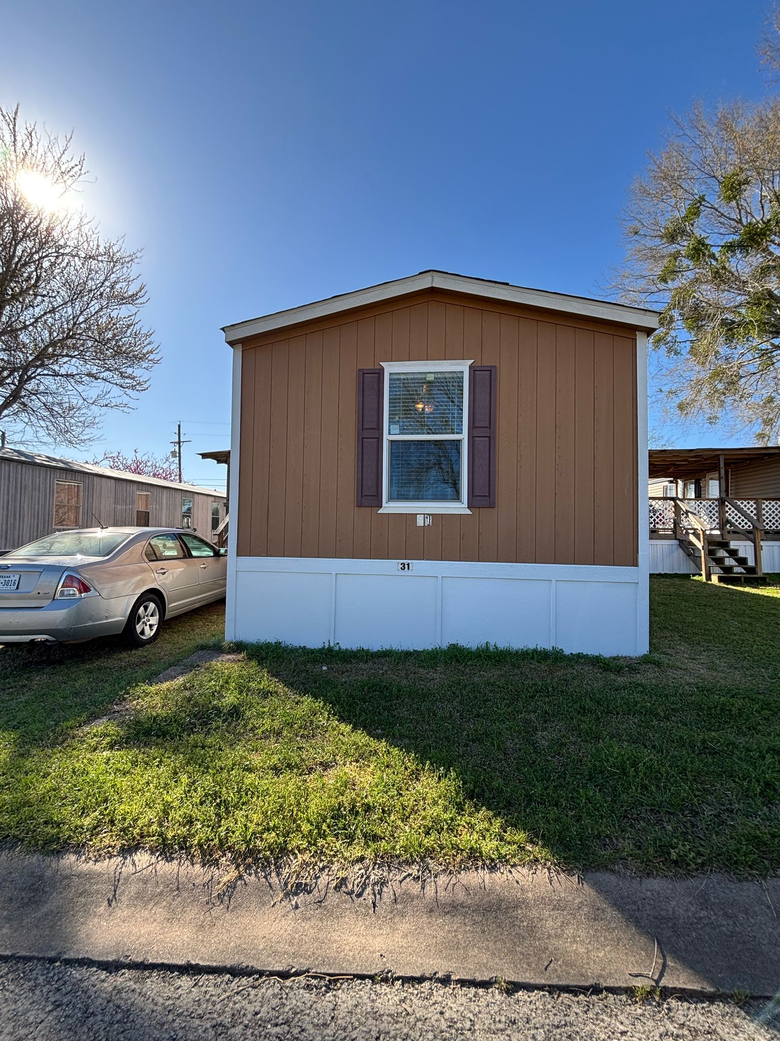 Brown and white mobile home with a beige car parked beside it.