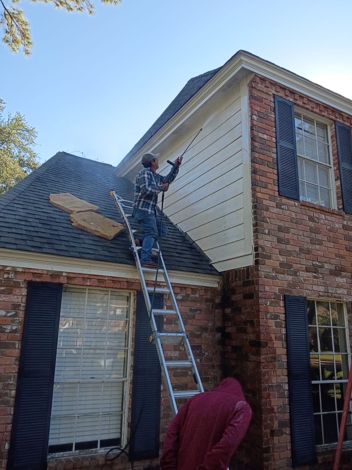 Man on ladder painting house siding.