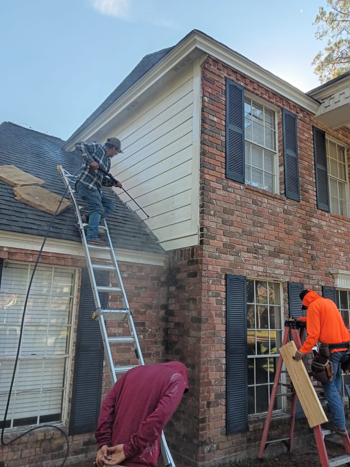 Workers repairing the exterior of a brick and siding house using ladders.