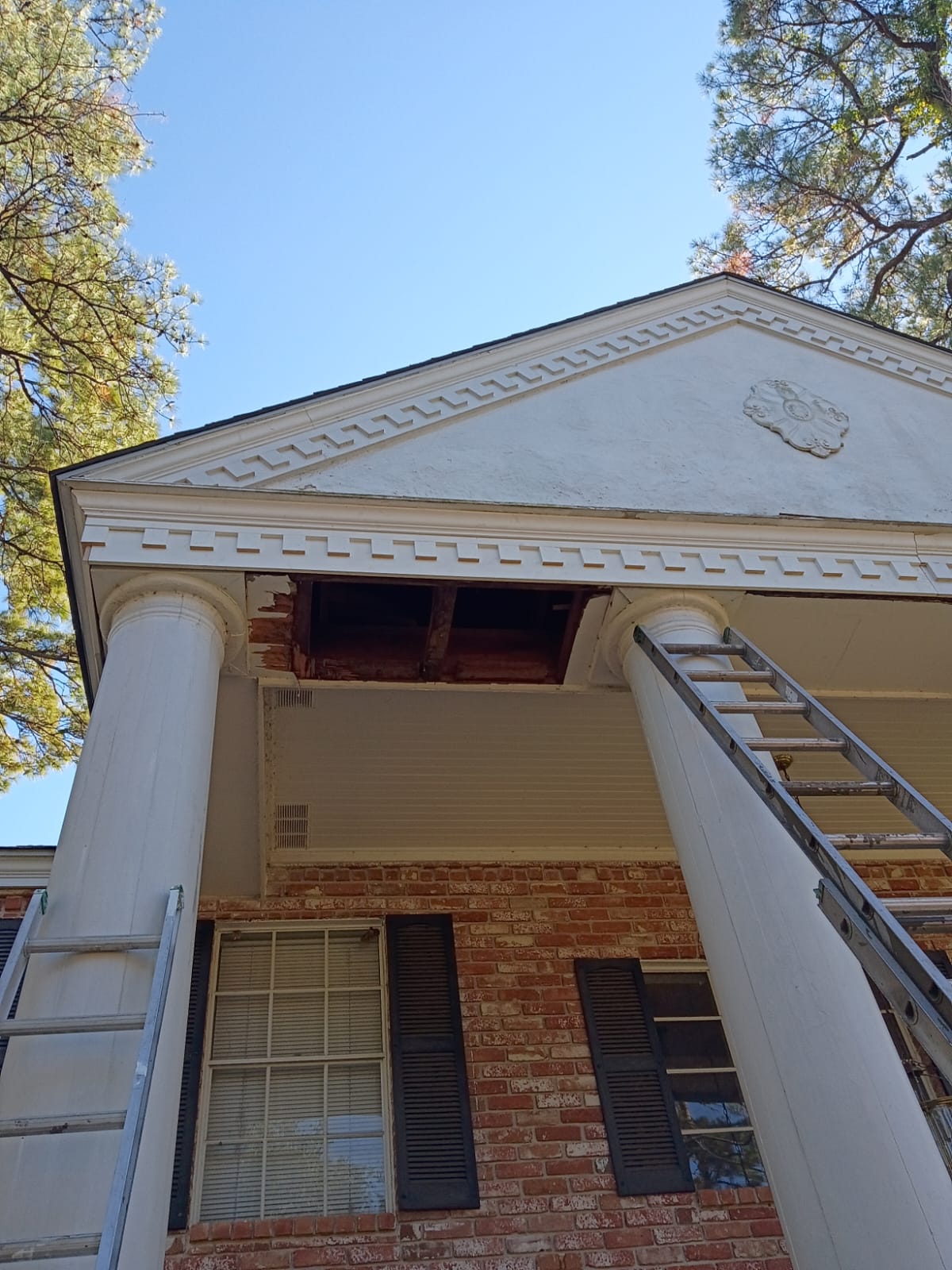 A ladder leaning against a white-columned porch under a blue sky.